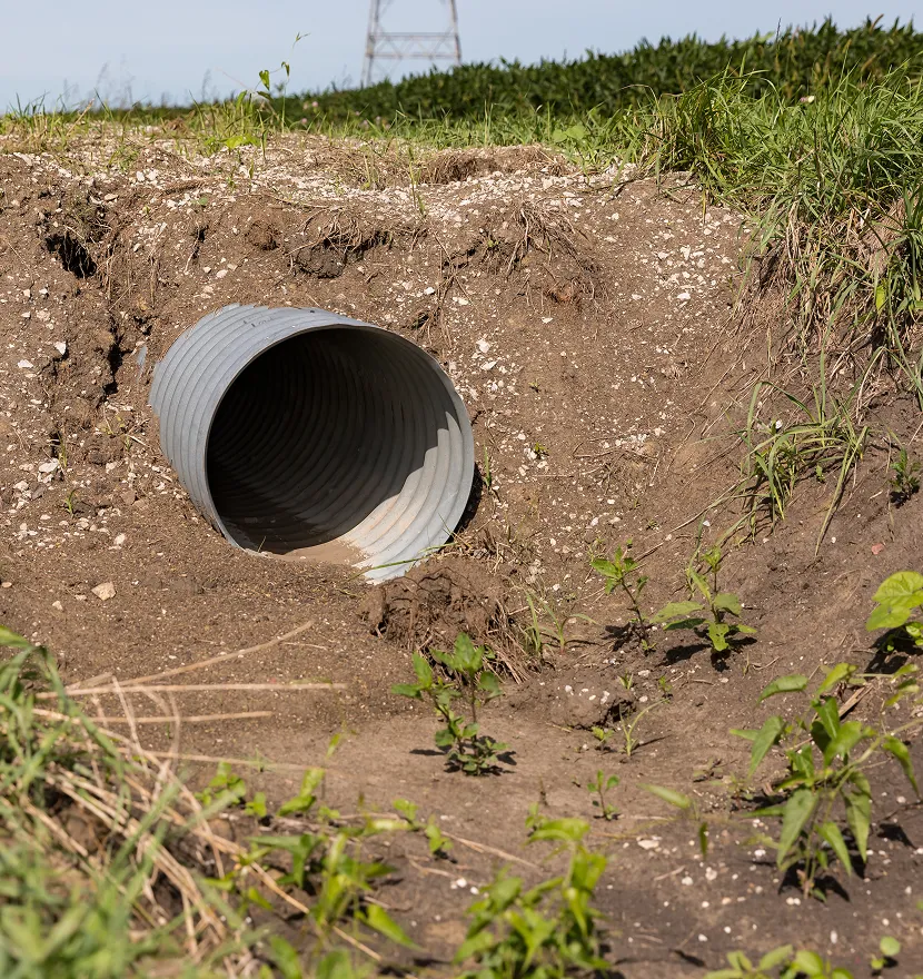 Metal drainage pipe in a grassy field.