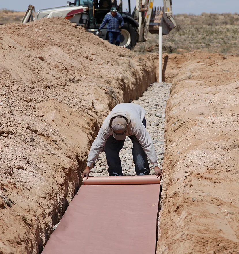 Worker laying fabric in a trench.