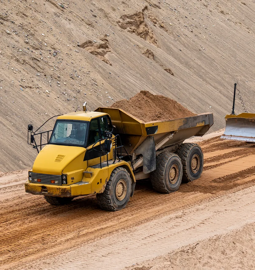 Yellow dump truck carrying sand on road.