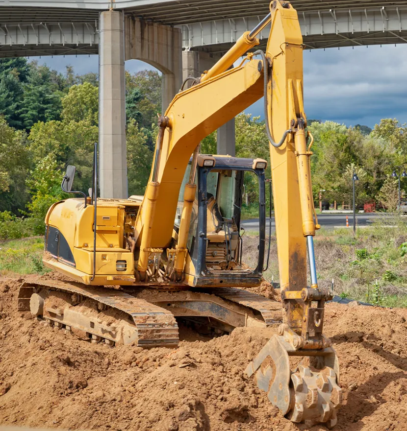 Yellow excavator on dirt under bridge.