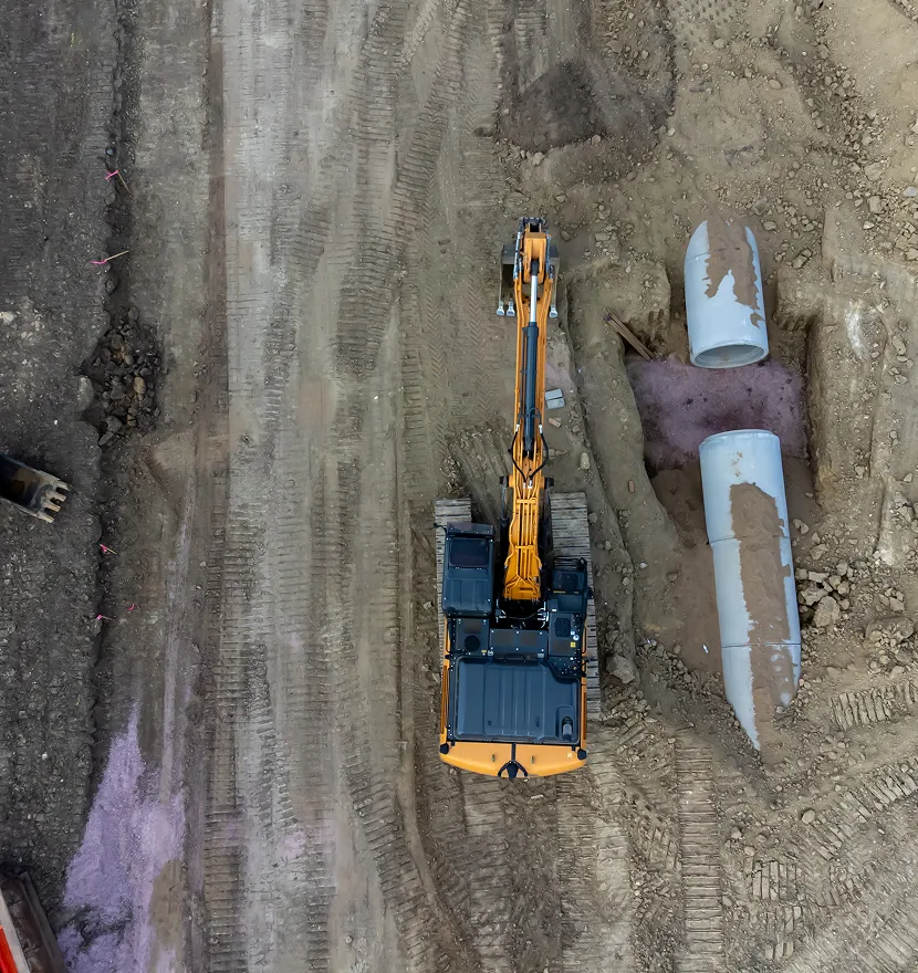 Excavator working on construction site with pipes.